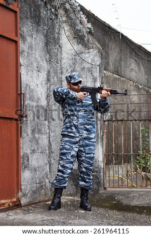 Caucasian man with black sunglasses in urban warfare holding rifle near gate