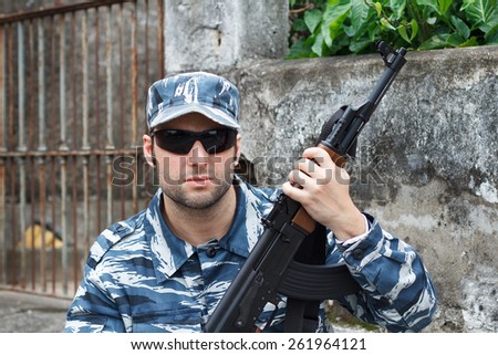 Portrait of military caucasian man with black sunglasses in urban warfare holding machine gun