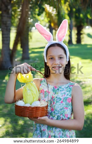 Smiling cute teen girl with rabbit ears holding chocolate eggs in colorful paper for Easter holiday in park. Selective focus on face