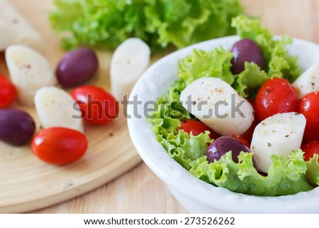 Fresh salad of heart of palm (palmito), cherry tomatoes and olives on white plate. Selective focus