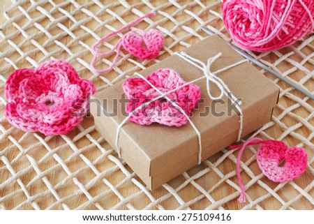 Handmade pink crochet flowers and heart for decoration of gift with skein on wooden table. Selective focus