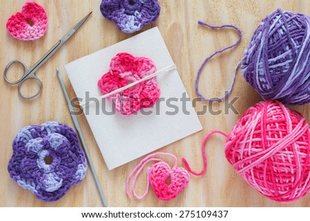 Handmade colorful crochet flowers and heart for decoration of greetings card with skein and scissors on wooden table. Selective focus