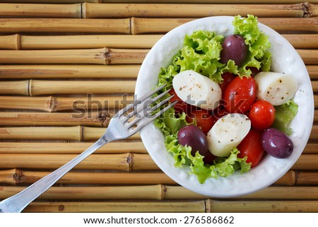 Fresh salad of heart of palm (palmito), cherry tomatoes, olives, black pepper on white plate with fork on bamboo. Selective focus. Copy space