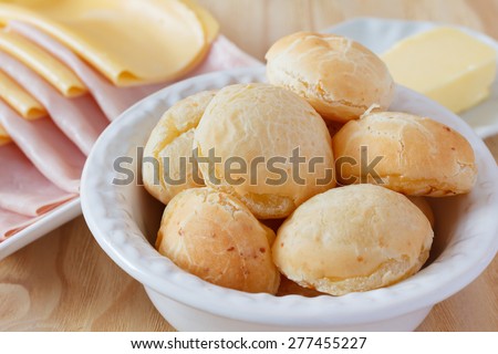 Brazilian snack pao de queijo (cheese bread) on white plate with cheese, ham, butter on wooden table. Selective focus