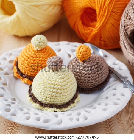 Handmade colorful crochet toys sweets on plate with skein on wooden table. Selective focus