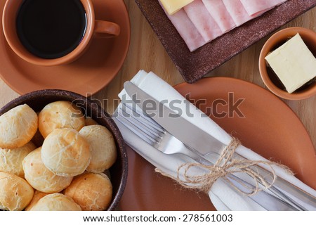 Brazilian snack pao de queijo (cheese bread) on brown plate with butter, cheese, ham, cup of coffee on wooden table. Selective focus