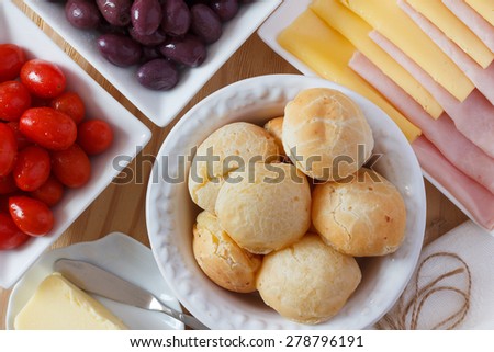 Brazilian snack pao de queijo (cheese bread) on white plate with cheese, ham, butter, cherry tomato and olives on wooden table. Selective focus
