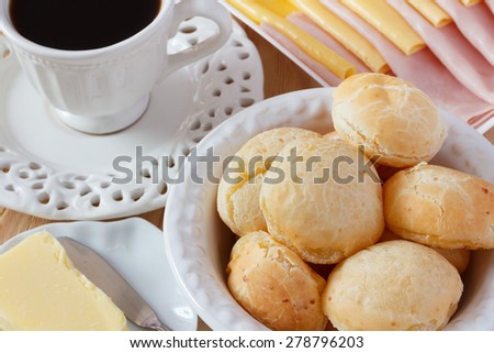 Brazilian snack pao de queijo (cheese bread) on white plate with cheese, ham, butter, cup of coffee on wooden table. Selective focus