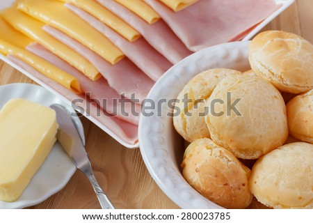 Brazilian snack pao de queijo (cheese bread) on white plate with cheese, ham, butter on wooden table. Selective focus
