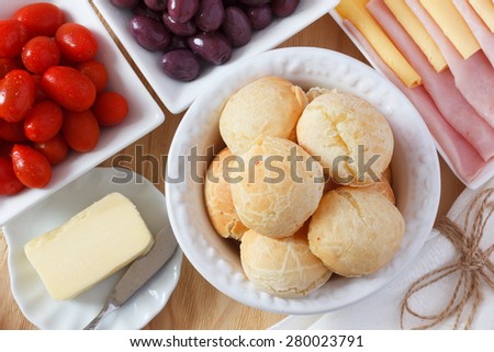 Brazilian snack pao de queijo (cheese bread) on white plate with cheese, ham, butter, cherry tomato and olives on wooden table. Selective focus