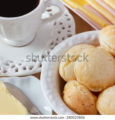 Brazilian snack pao de queijo (cheese bread) on white plate with cheese, ham, butter, cup of coffee on wooden table. Selective focus