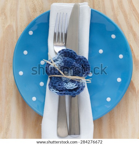 Blue plate with serviette, fork, knife and handmade crochet flower for table decoration. Selective focus