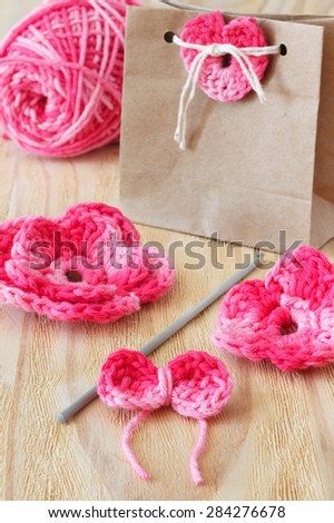 Handmade pink flowers, heart and bow for decoration of gift with skein on wooden table. Selective focus