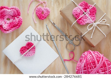 Handmade pink crochet flowers and heart for decoration of gift and greetings card with skein on wooden table. Selective focus