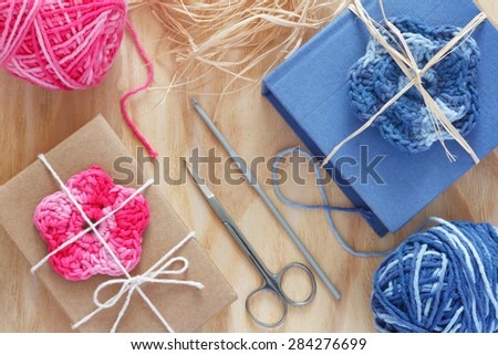 Handmade pink and blue crochet flowers for decoration of gift with skein on wooden table. Selective focus