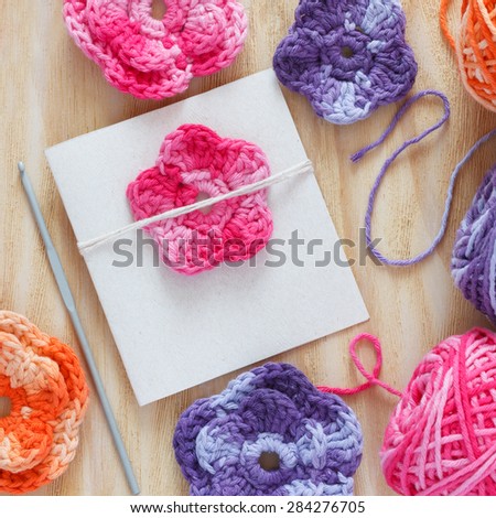 Handmade colorful crochet flowers and heart for decoration of greetings card with skein on wooden table. Selective focus