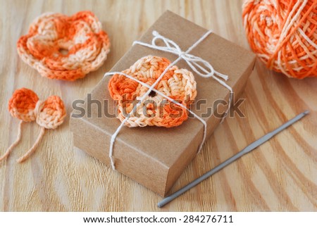 Handmade orange crochet flowers and bow for decoration of gift with skein on wooden table. Selective focus
