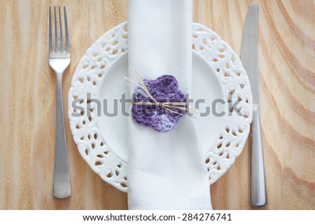 White vintage plate with serviette, fork, knife and handmade crochet purple flower for decoration. Selective focus