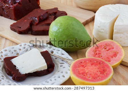 Brazilian dessert Romeo and Juliet on white plate, goiabada and Minas cheese with fresh goiaba on wooden table. Selective focus