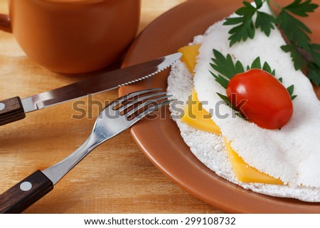 Casabe (bammy, beiju, bob, biju) - flatbread made from cassava (tapioca) with cheese, cherry tomato and parsley on brown plate with coffee. Selective focus