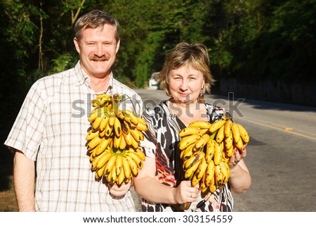 Couple Man and woman smiling and holding butch of bananas near road. Selective focus