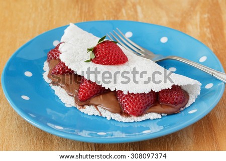 Casabe (bammy, beiju, bob, biju) - flatbread made from cassava (tapioca) with strawberry and chocolate spread on blue plate on wooden table. Selective focus