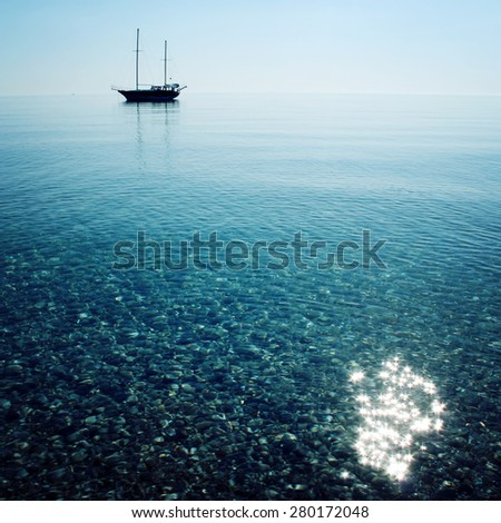 Morning sea with boat on the horizon. Aged photo. Sailing ship profile. Toned image. Sunbeams on the sea surface. Calm Sea with a Sailing Vessel. Cirali, Antalya Province, Turkey.
