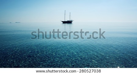 Sailing ship profile. Toned image. Sunbeams on the sea surface. Morning sea with boat on the horizon. Aged photo. Calm Sea with a Sailing Vessel. Cirali, Antalya Province, Turkey. soft focus.