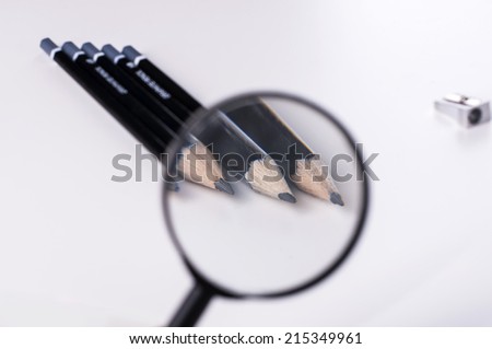 black pencils and pencil-sharpener under magnifying glass