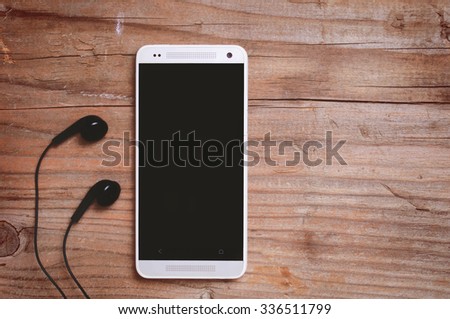 Cell phone and headphones on wooden table, blank space