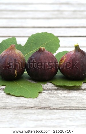 Three purple figs on a fig leaf and wooden table background