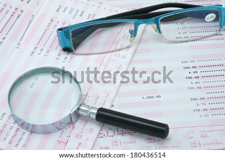 Magnifier and spectacles are on pink and white bank account.