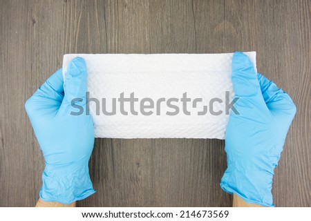 Man wear blue latex gloves holding tissue paper on wood background.