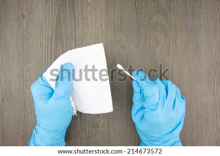 Man wear purple latex gloves holding cotton bud and tissue paper on wood background.