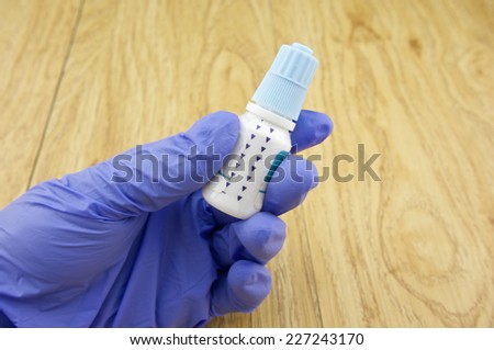 Hand wear latex glove holding blue eye drop with wood background.