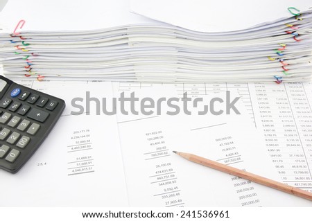 Balance sheet with pencil and calculator on finance account with pile of paperwork as background.