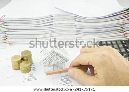 Man is holding pencil horizon over balance sheet with pile of paperwork as background.