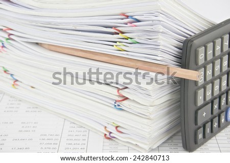 Brown pencil put in stack paperwork with vertical calculator on finance account with pile of paperwork as background.
