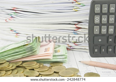 Stack bill, gold coins, brown pencil and calculator on finance account with pile of paperwork as background.