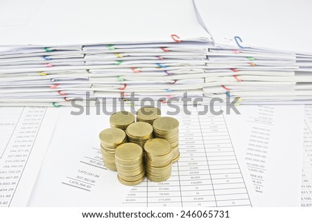 Stack of gold coins on finance account with pile of paperwork as background.
