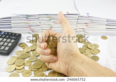 Gold coins in hand signal by thumb on finance account with pile of paperwork as background.
