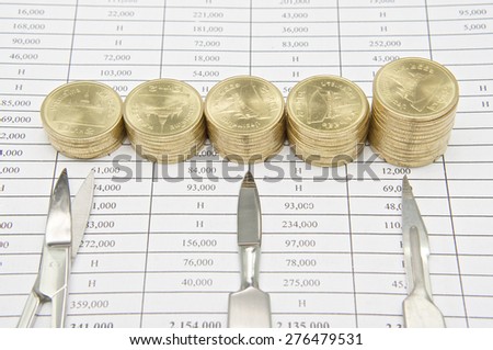 Scalpel and surgical scissors with step pile of gold coins on finance report.