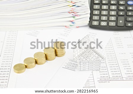 Step pile of gold coins and house on balance sheet have calculator and pile of paperwork as background.