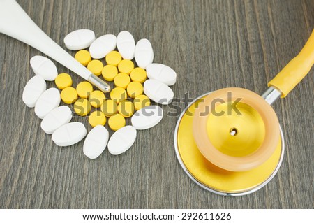 Close up gold stethoscope and pile of pills for painkiller with digital thermometer.