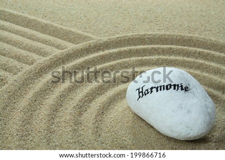 stone onto sand with patterns and the German word Harmonie means harmony