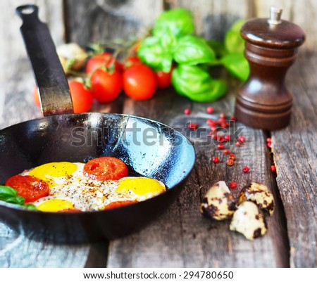 Scrambled eggs with tomatoes and basil in the black pan on the old wooden table