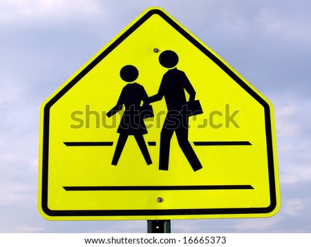 Black on yellow school crossing sign isolated against blue sky background