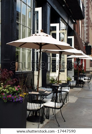 Outdoor cafe tables with umbrellas up and places set waiting for customers to arrive