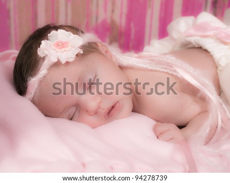 Beautiful newborn girl asleep in her bed with white ruffled bloomers with a pink bow and beautiful headband of yarn and ribbon and a fabric pink flower,