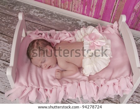 One week old newborn baby girl with white bloomers and a pink bow is fast asleep in her bed.